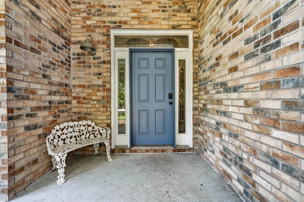 A blue front door with sidelights and a white metal bench on a brick porch — 16 REGENCY DRIVE, PALM COAST, FL