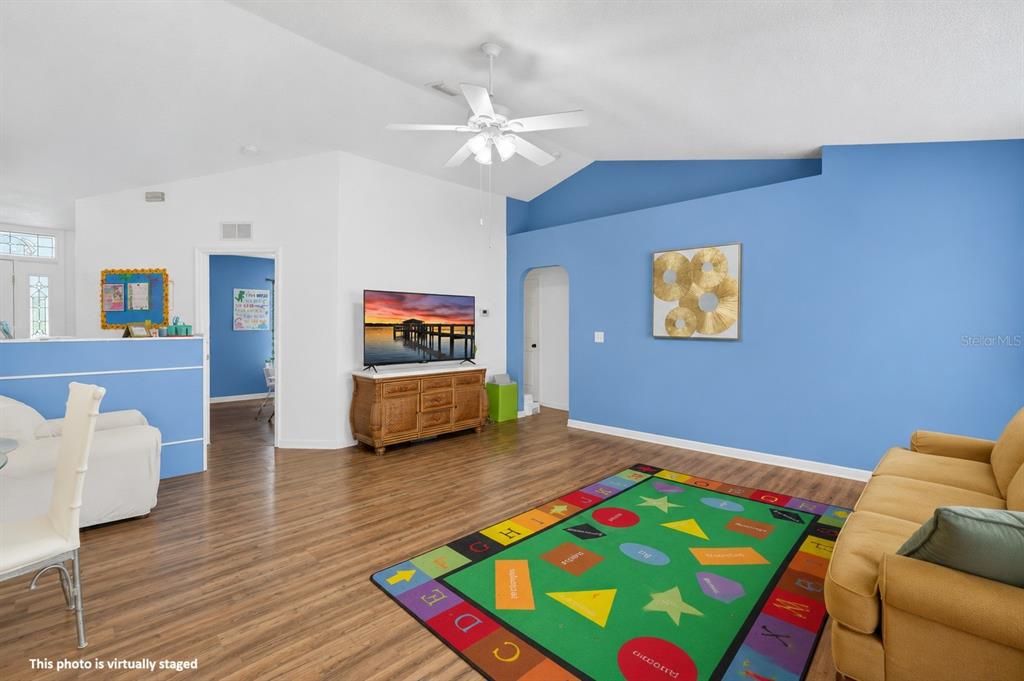 A living room features wood-look flooring, a blue accent wall, and a colorful alphabet rug — 16 REGENCY DRIVE, PALM COAST, FL
