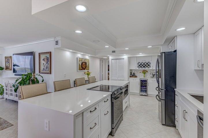 A modern white kitchen features a large island with a cooktop and stainless steel appliances — 5440 N Ocean Drive # 1502, Singer Island FL 33404, SINGER ISLAND, FL