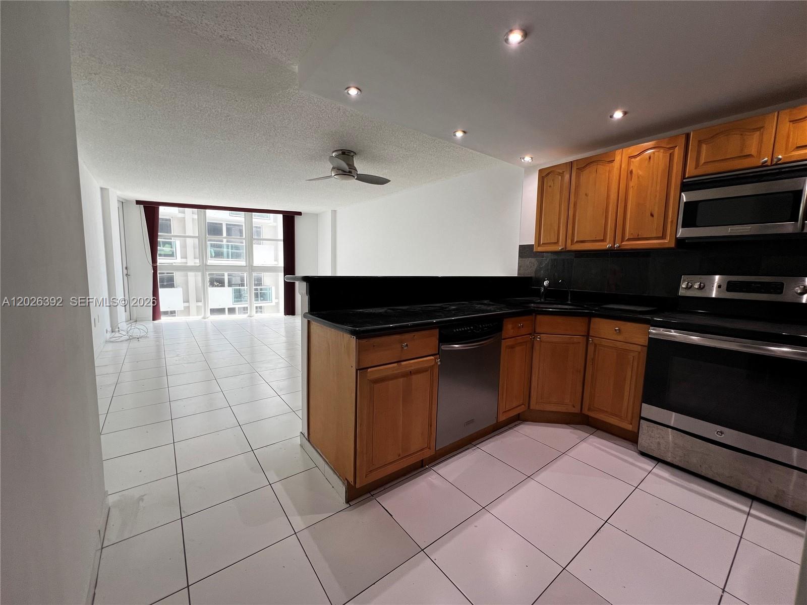 A kitchen with wood cabinets and black countertops opens into a tiled living area — 1228 West Ave # 1114, Miami Beach FL 33139, MIAMI BEACH, FL