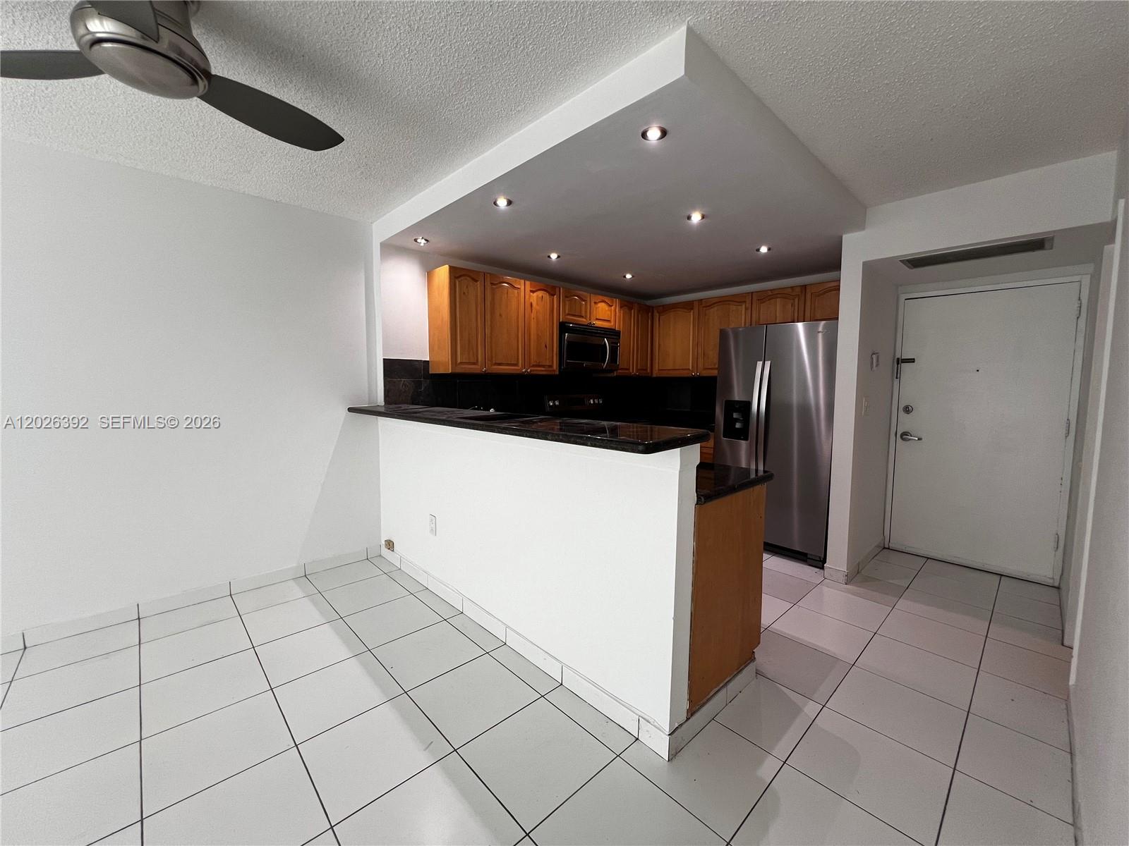 A kitchen features wooden cabinets, stainless steel appliances, and a breakfast bar over tiled floors — 1228 West Ave # 1114, Miami Beach FL 33139, MIAMI BEACH, FL
