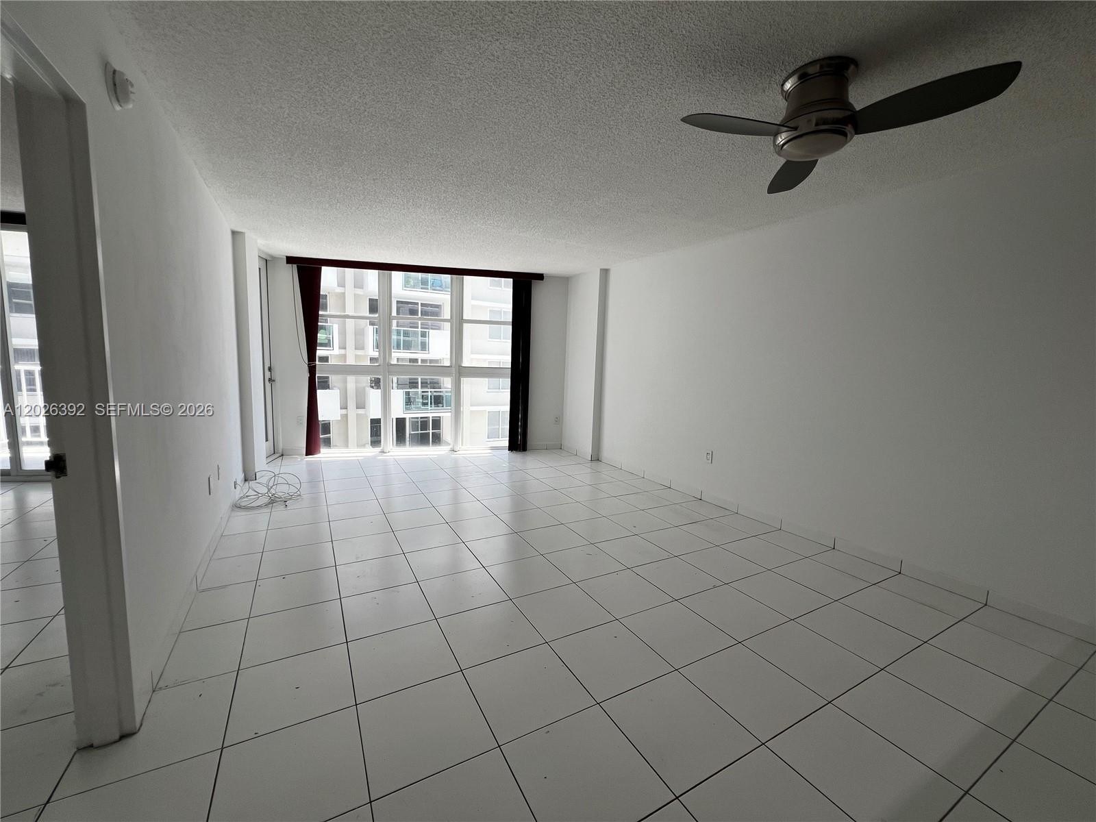 An empty room features white tile flooring, a ceiling fan, and large floor-to-ceiling windows — 1228 West Ave # 1114, Miami Beach FL 33139, MIAMI BEACH, FL