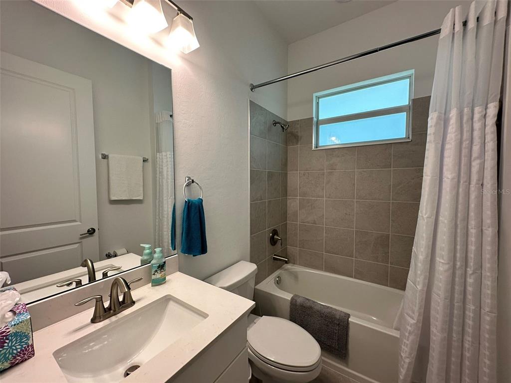 A bathroom features a white vanity, a toilet, and a tub-shower combo with tiled walls — 13372 JOURNAL LANE, PORT CHARLOTTE, FL