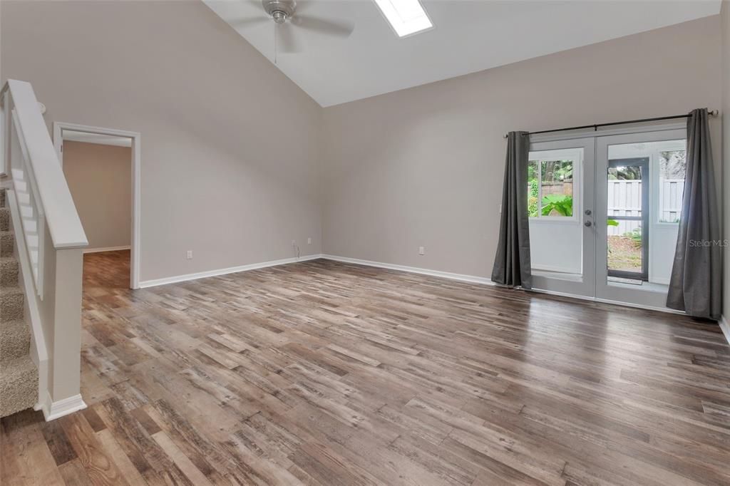 An empty living room features vaulted ceilings, wood-look flooring, a ceiling fan, and glass doors — 2919 REVERE PLACE UNIT 2919, DELAND, FL