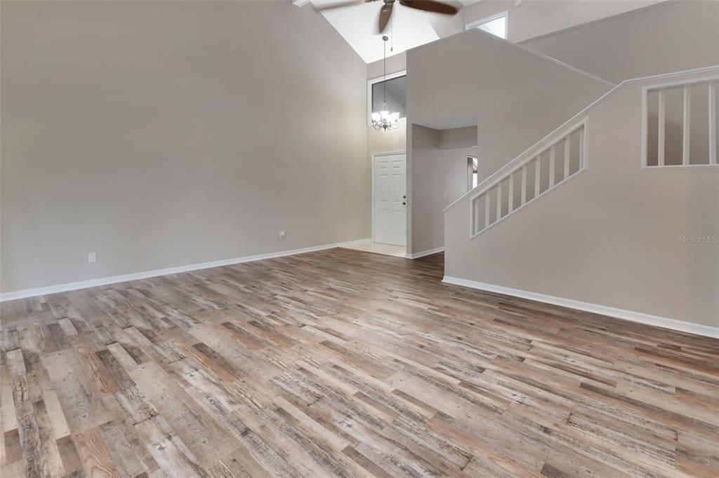 A living room features high vaulted ceilings, wood-look flooring, and a staircase with white railings — 2919 REVERE PLACE UNIT 2919, DELAND, FL