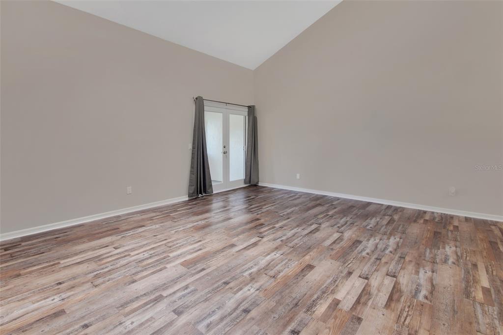 An empty room features wood-look flooring, light gray walls, and glass double doors with curtains — 2919 REVERE PLACE UNIT 2919, DELAND, FL