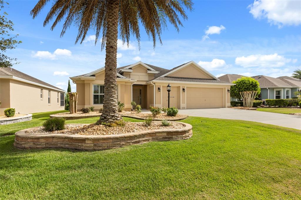 A single-story tan house with a palm tree and stone-bordered landscaping in the front yard — 842 PICKETT ROAD, THE VILLAGES, FL