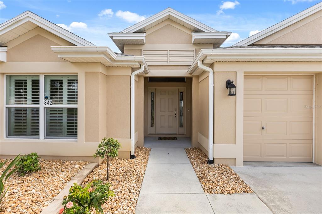 The exterior of a tan house features a front entrance, a garage, and gravel landscaping — 842 PICKETT ROAD, THE VILLAGES, FL
