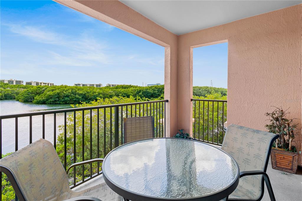 A balcony with a glass-topped table and chairs overlooks a body of water and trees — 2729 VIA MURANO DRIVE UNIT 429, CLEARWATER, FL