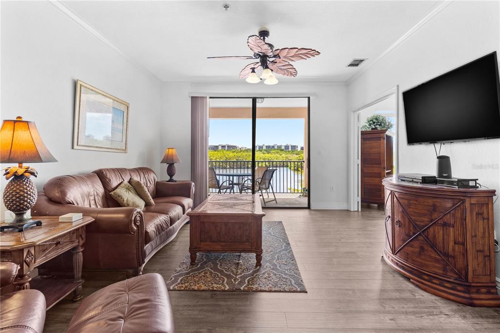 A living room features a brown leather sofa, wood furniture, tile flooring, and a balcony view — 2729 VIA MURANO DRIVE UNIT 429, CLEARWATER, FL
