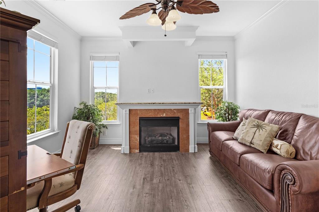 A living room features a fireplace, a leather sofa, wood-look flooring, and a ceiling fan — 2729 VIA MURANO DRIVE UNIT 429, CLEARWATER, FL