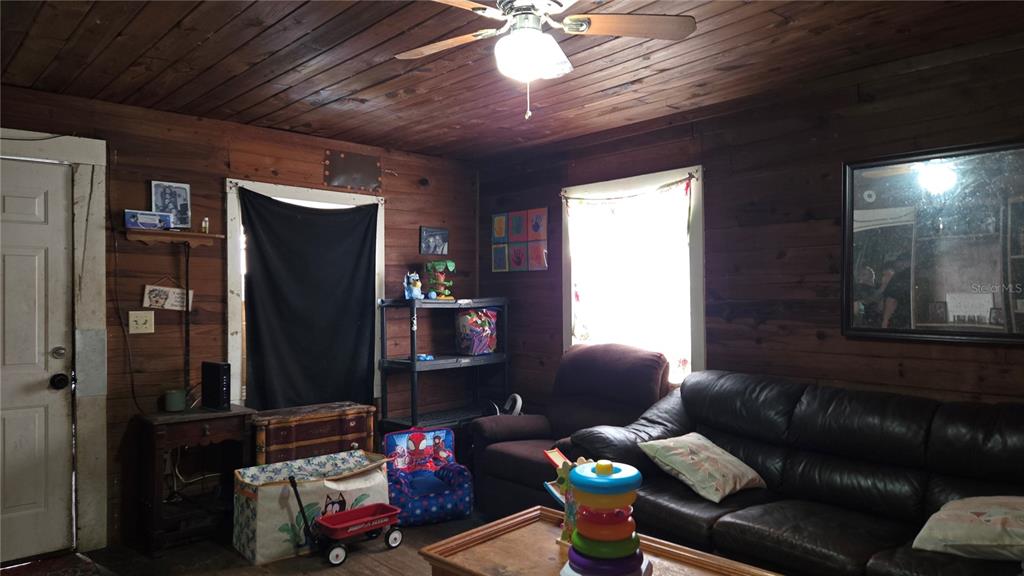A living room features wood-paneled walls, a ceiling fan, a leather sofa, and children's toys — 883 NE MAPLE LANE, LAKE CITY, FL