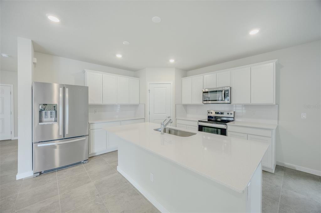 A modern kitchen features white cabinetry, stainless steel appliances, and a central quartz island — 6107 WOODED BRUSH ALLEY, ST CLOUD, FL