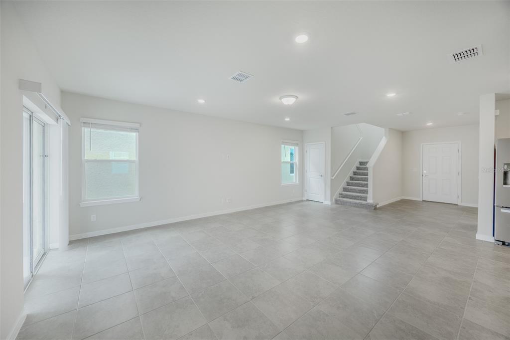 An open-concept living area features light gray tile flooring, white walls, and a staircase — 6107 WOODED BRUSH ALLEY, ST CLOUD, FL
