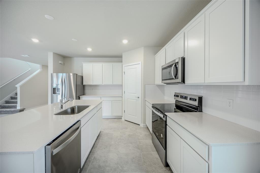 A modern kitchen features white cabinetry, stainless steel appliances, and a central island with sink — 6107 WOODED BRUSH ALLEY, ST CLOUD, FL
