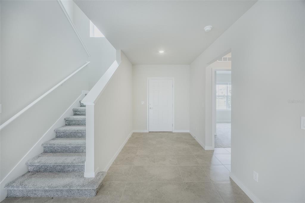 An entryway features light-colored tile flooring, a carpeted staircase, and a white front door — 6107 WOODED BRUSH ALLEY, ST CLOUD, FL
