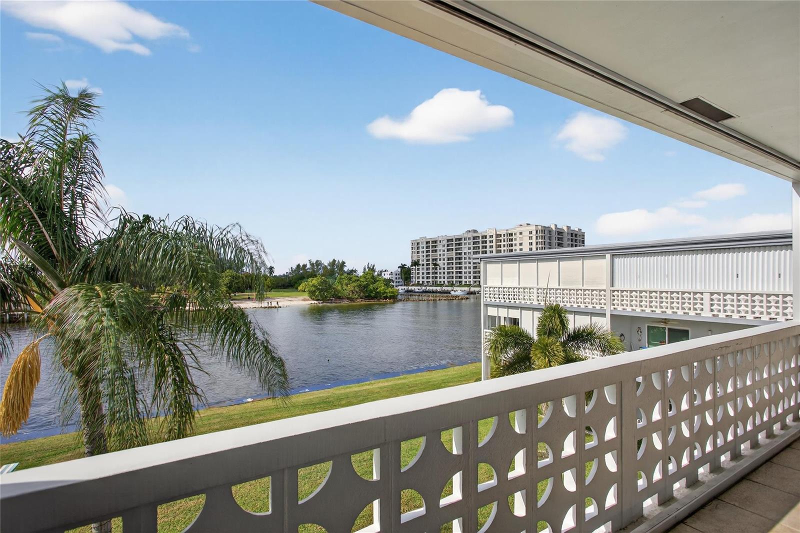 A balcony with a decorative white railing overlooks a waterfront view with palm trees — 1001 N Riverside Drive # 305, Pompano Beach FL 33062, POMPANO BEACH, FL