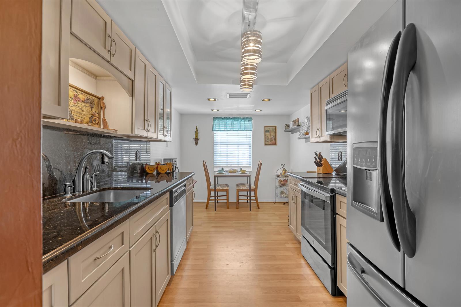 A galley kitchen features light-colored cabinets, dark granite countertops, stainless steel appliances, and a dining area — 1250 Sugar Sands Boulevard # 207, Singer Island FL 33404, SINGER ISLAND, FL