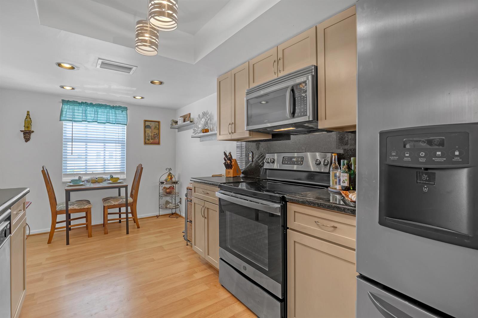 A kitchen features light wood cabinets, stainless steel appliances, dark countertops, and an adjacent dining area — 1250 Sugar Sands Boulevard # 207, Singer Island FL 33404, SINGER ISLAND, FL