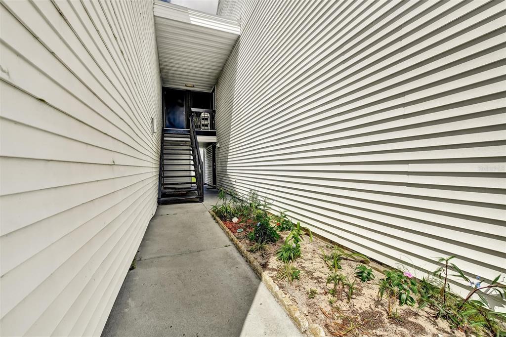 A concrete walkway leads to a metal staircase between two white vinyl-sided building walls — 704 HAVEN PLACE UNIT 704, TARPON SPRINGS, FL