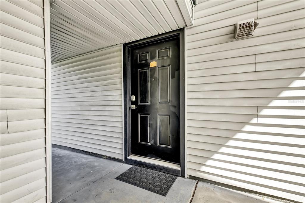 A black front door with a small address plaque sits on a concrete porch — 704 HAVEN PLACE UNIT 704, TARPON SPRINGS, FL