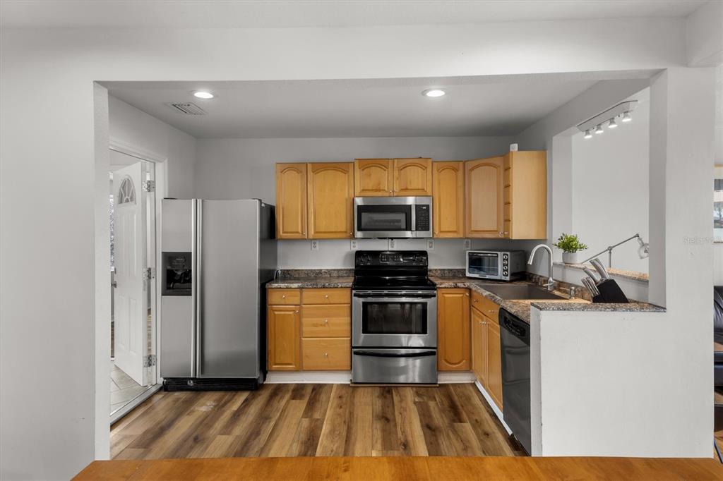 A kitchen features wood cabinets, stainless steel appliances, granite countertops, and wood-look flooring — 900 LAKE JESSIE DRIVE, WINTER HAVEN, FL