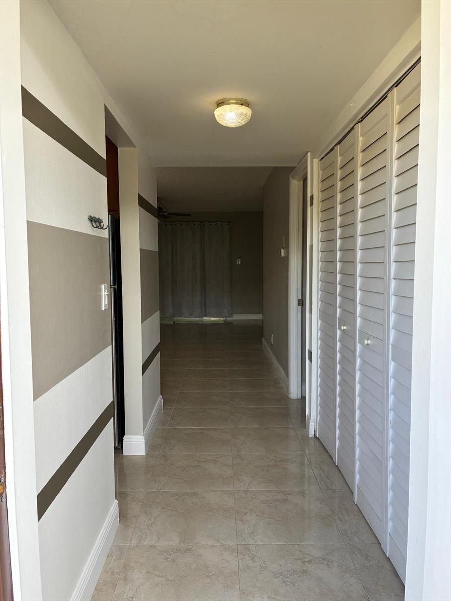 A hallway with beige and white striped walls, tile flooring, and white louvered closet doors — 7300 NW 5th Court # 106, Margate FL 33063, MARGATE, FL
