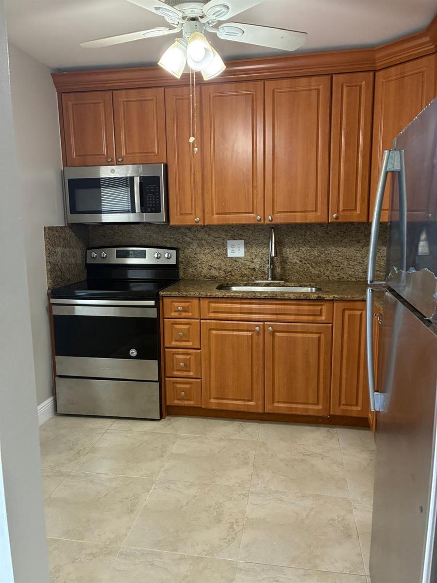 A kitchen features wood cabinets, stainless steel appliances, granite countertops, and light-colored tile flooring — 7300 NW 5th Court # 106, Margate FL 33063, MARGATE, FL