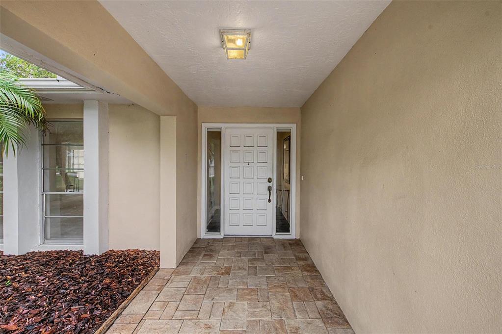 A covered entryway features a white front door with glass panels and stone-look tile flooring — 14317 110TH TERRACE, LARGO, FL