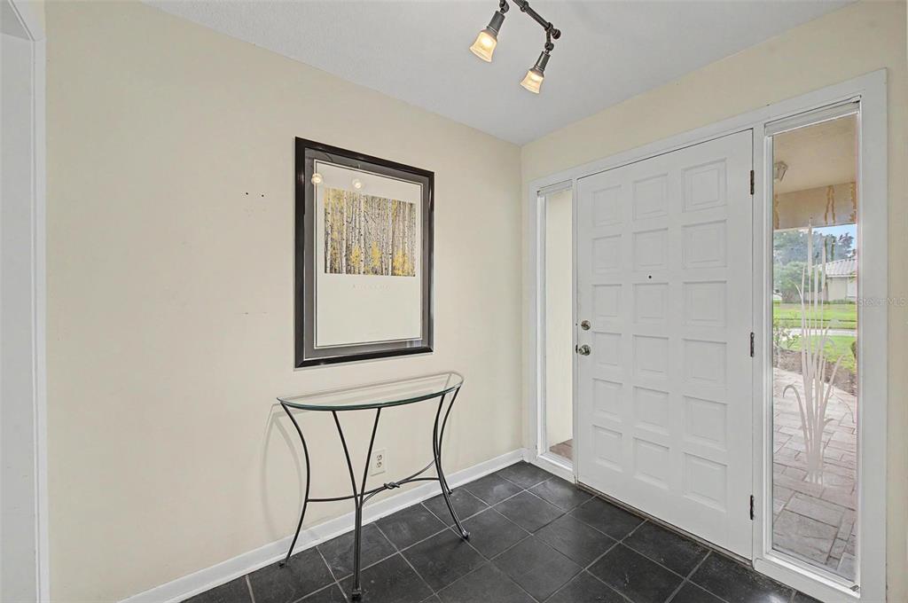 An entryway features dark tile flooring, a glass console table, wall art, and a white door — 14317 110TH TERRACE, LARGO, FL