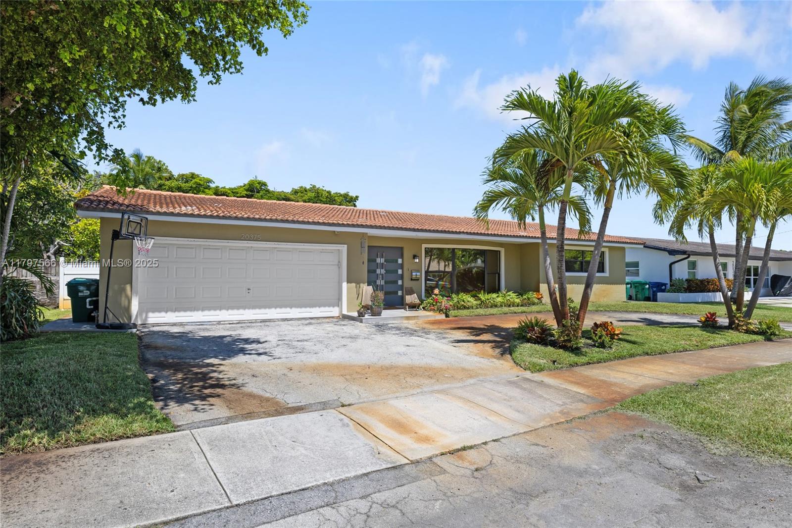 A single-story house with a two-car garage, tile roof, and palm trees in the front yard — 20375 NE 22nd Pl, Miami FL 33180, MIAMI, FL