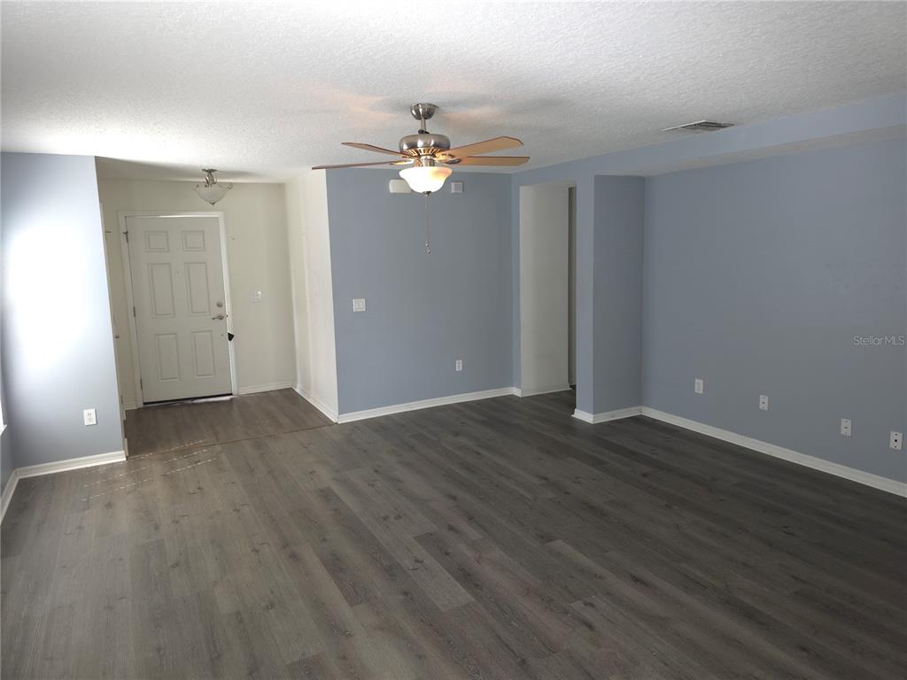An empty living room features light blue walls, dark wood-look flooring, and a ceiling fan — 13812 CEPHEUS DRIVE, ORLANDO, FL