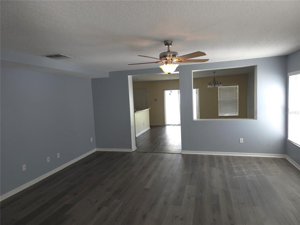 An empty living room features light blue walls, gray wood-look flooring, and a ceiling fan — 13812 CEPHEUS DRIVE, ORLANDO, FL