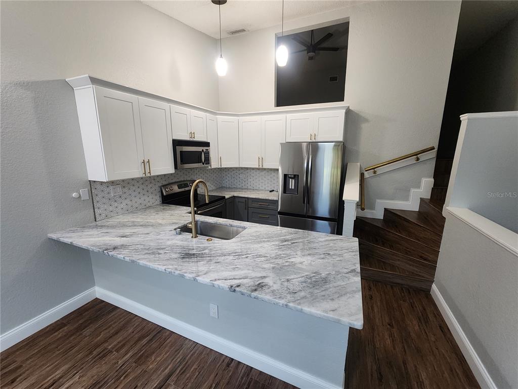 A kitchen features white upper cabinets, dark lower cabinets, marble-look countertops, and a staircase nearby — 6236 93RD TERRACE N UNIT 3504, PINELLAS PARK, FL