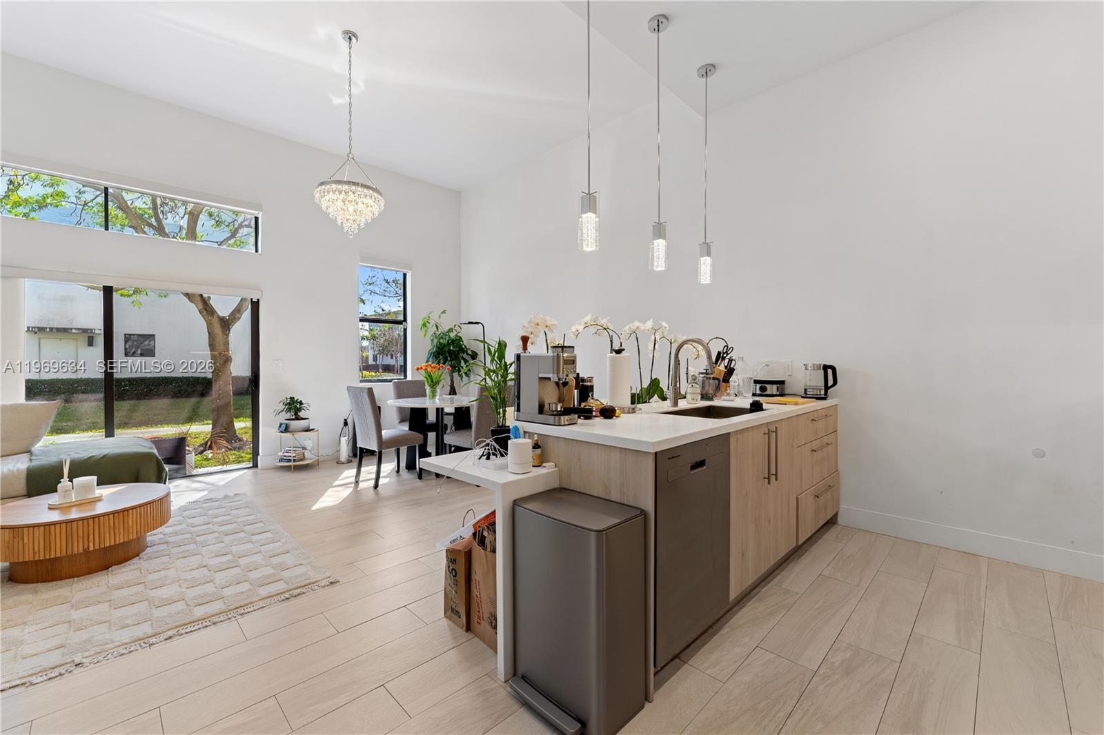 A modern kitchen with light wood cabinets and a central island opens to a living area — 4440 NW 8th Ct, Plantation FL 33317, PLANTATION, FL