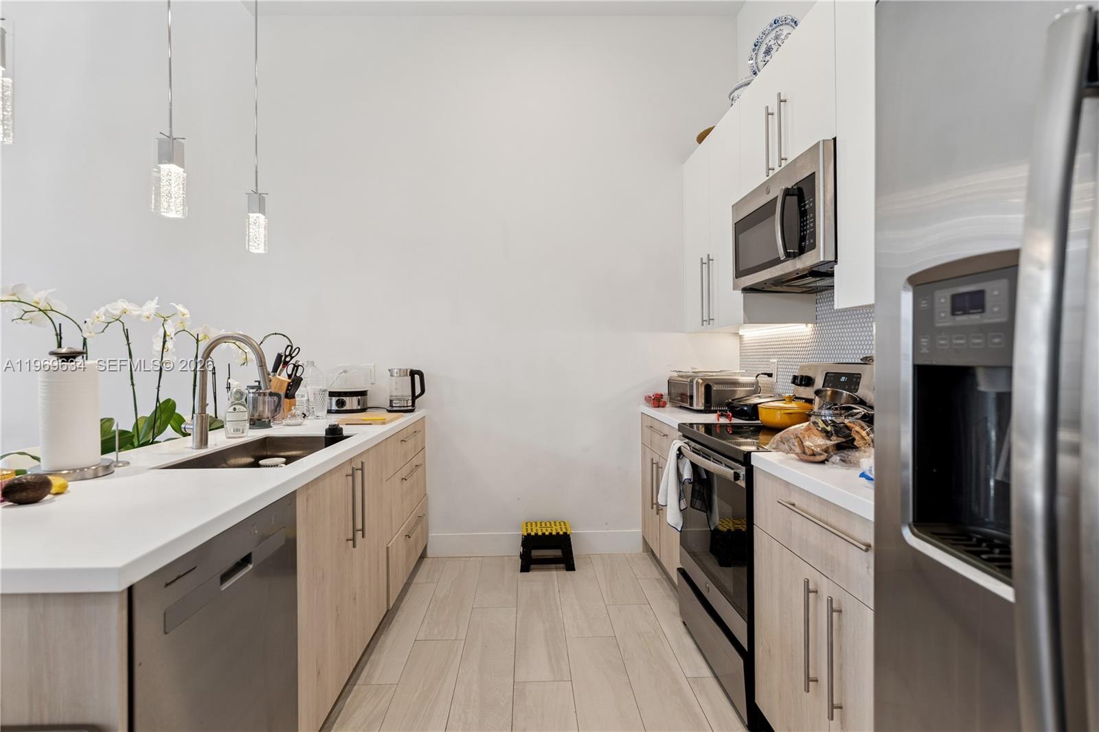 A galley-style kitchen features light wood cabinetry, white countertops, stainless steel appliances, and tile flooring — 4440 NW 8th Ct, Plantation FL 33317, PLANTATION, FL