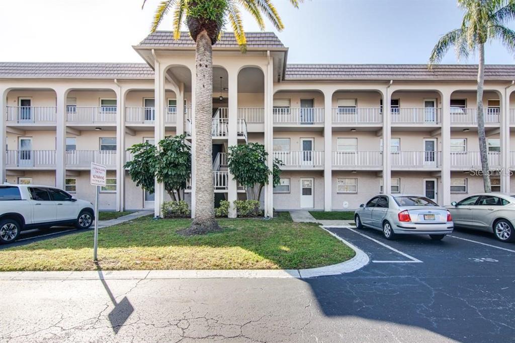 A three-story apartment building with a central staircase, palm trees, and a parking lot — 1303 S HERCULES AVENUE UNIT 19, CLEARWATER, FL