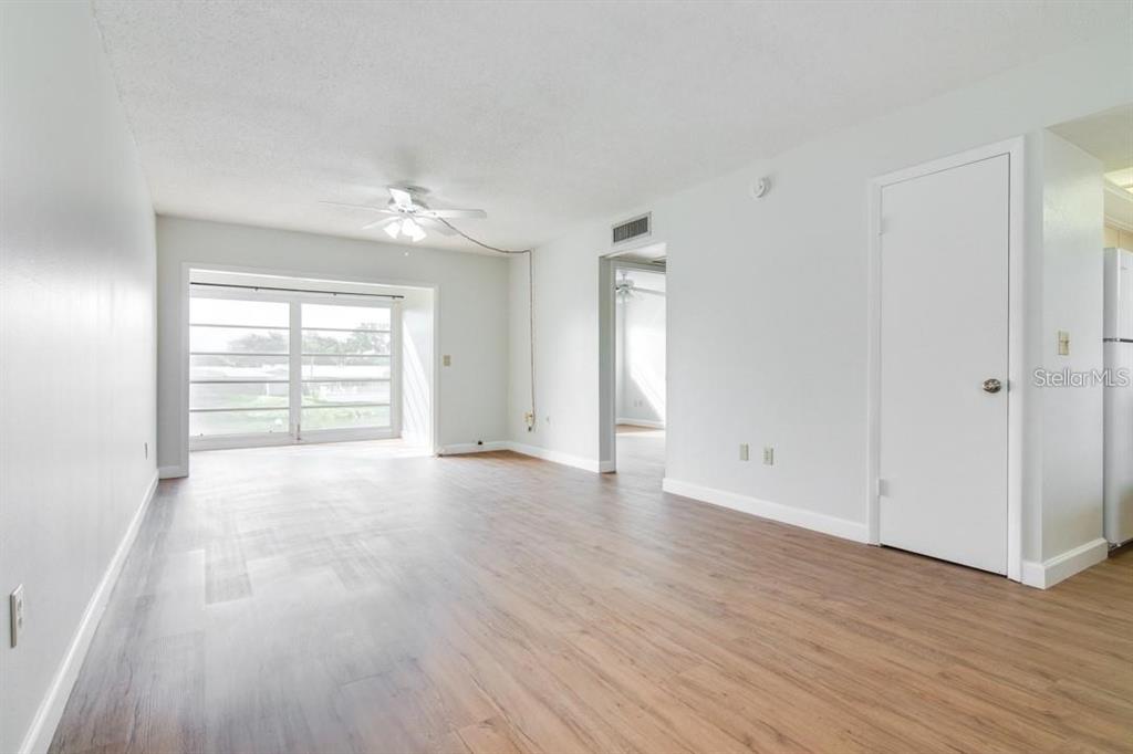A living room with light wood-look flooring, white walls, and a large sliding glass door — 1303 S HERCULES AVENUE UNIT 19, CLEARWATER, FL