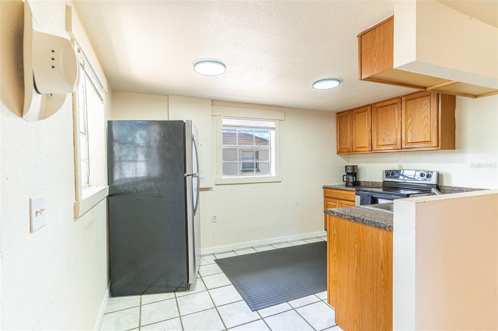 A kitchen features a black refrigerator, wooden cabinets, a stove, and white tiled flooring — 225 W NORTHSIDE DRIVE, LAKE WALES, FL