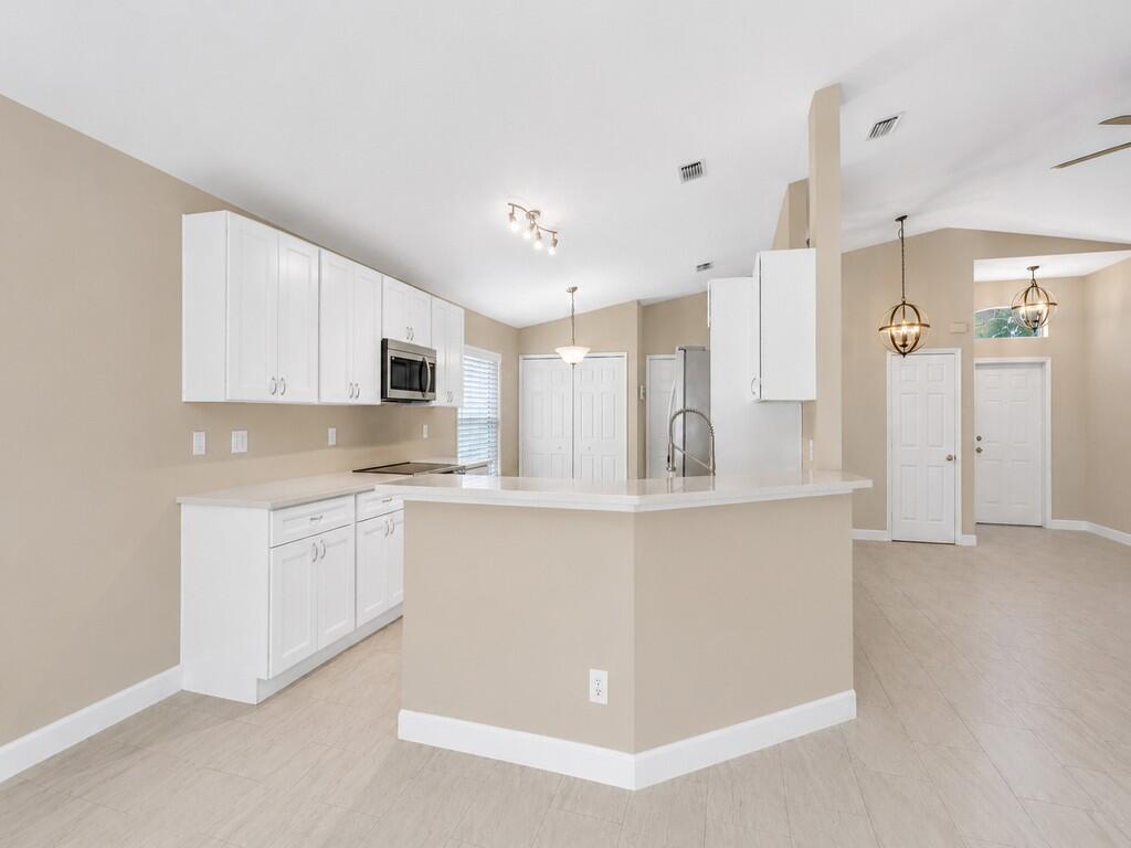 A kitchen with white cabinets, light countertops, and beige walls features a peninsula breakfast bar — 962 E 13th Square, Vero Beach FL 32960, VERO BEACH, FL