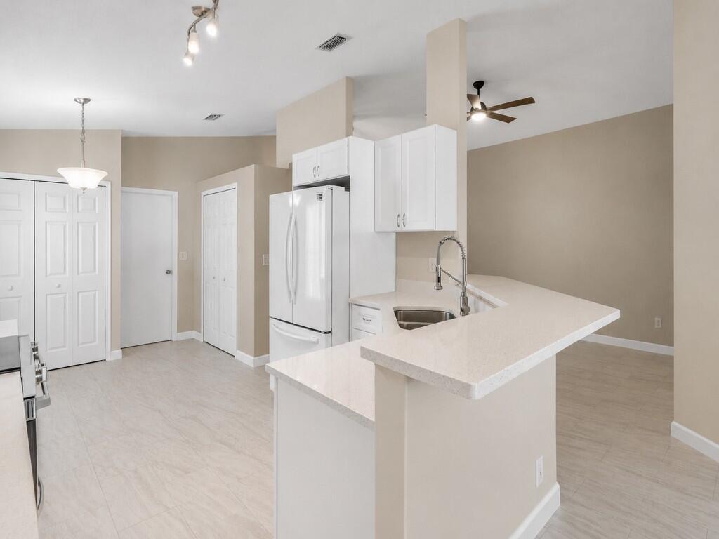 A kitchen with white cabinets, quartz countertops, a peninsula, and light-colored tile flooring — 962 E 13th Square, Vero Beach FL 32960, VERO BEACH, FL