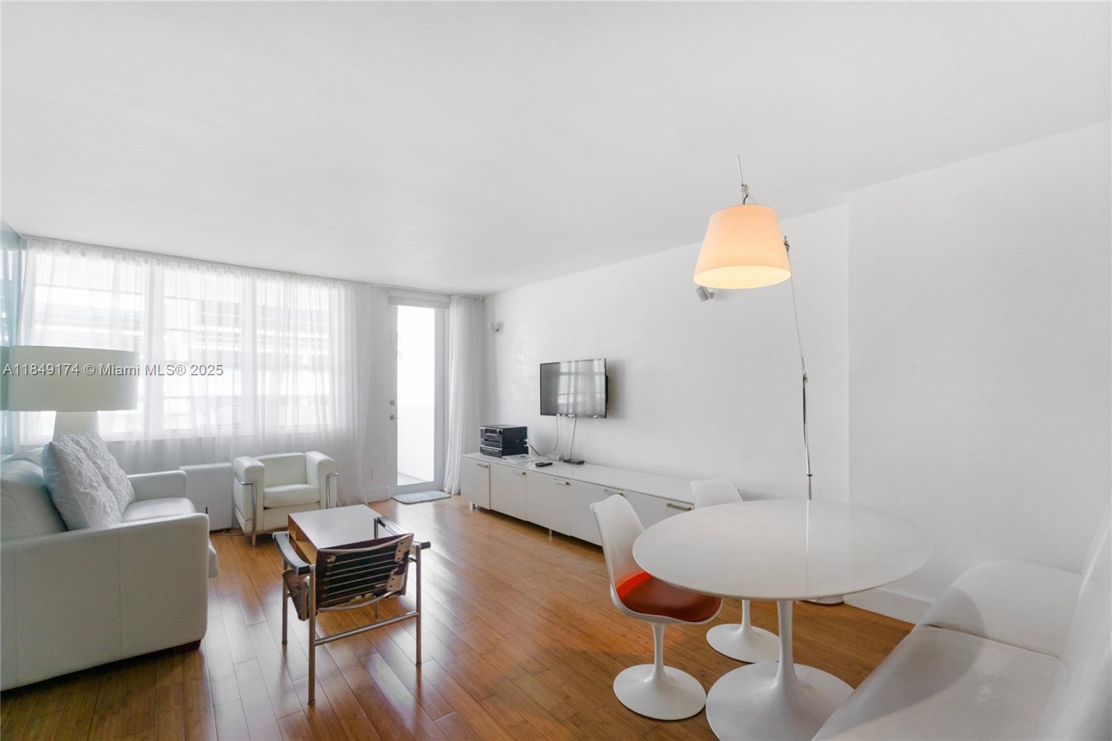 A bright living and dining room features white furniture, hardwood floors, and large windows — 100 Lincoln Rd # 923, Miami Beach FL 33139, MIAMI BEACH, FL