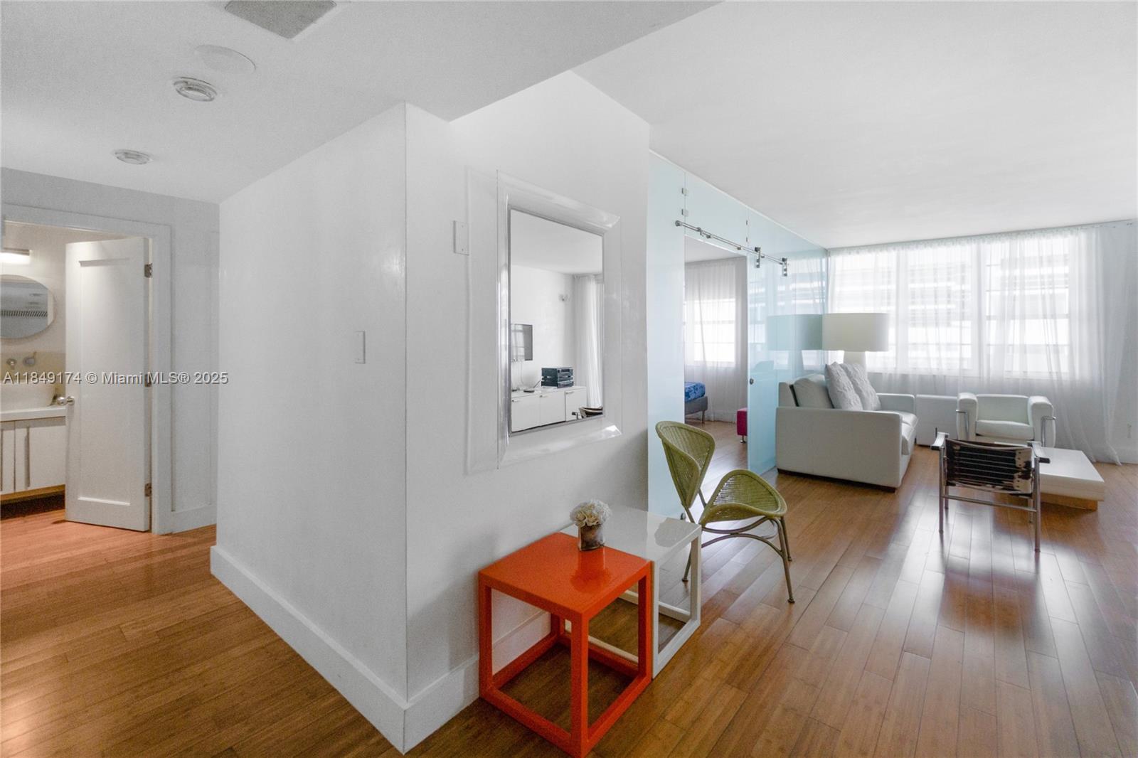 A living area with light wood floors, a glass partition, and a small orange table — 100 Lincoln Rd # 923, Miami Beach FL 33139, MIAMI BEACH, FL