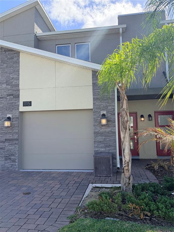 A two-story townhouse exterior features a single-car garage, stone veneer siding, and red doors — 1115 CHALLENGE DRIVE UNIT 1115, DAVENPORT, FL