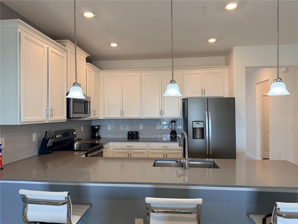 A kitchen features white cabinets, gray countertops, a subway tile backsplash, and three pendant lights — 1115 CHALLENGE DRIVE UNIT 1115, DAVENPORT, FL