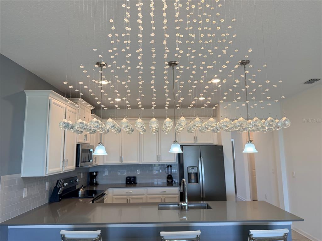 A kitchen features a large crystal chandelier hanging above a gray island with white cabinets — 1115 CHALLENGE DRIVE UNIT 1115, DAVENPORT, FL