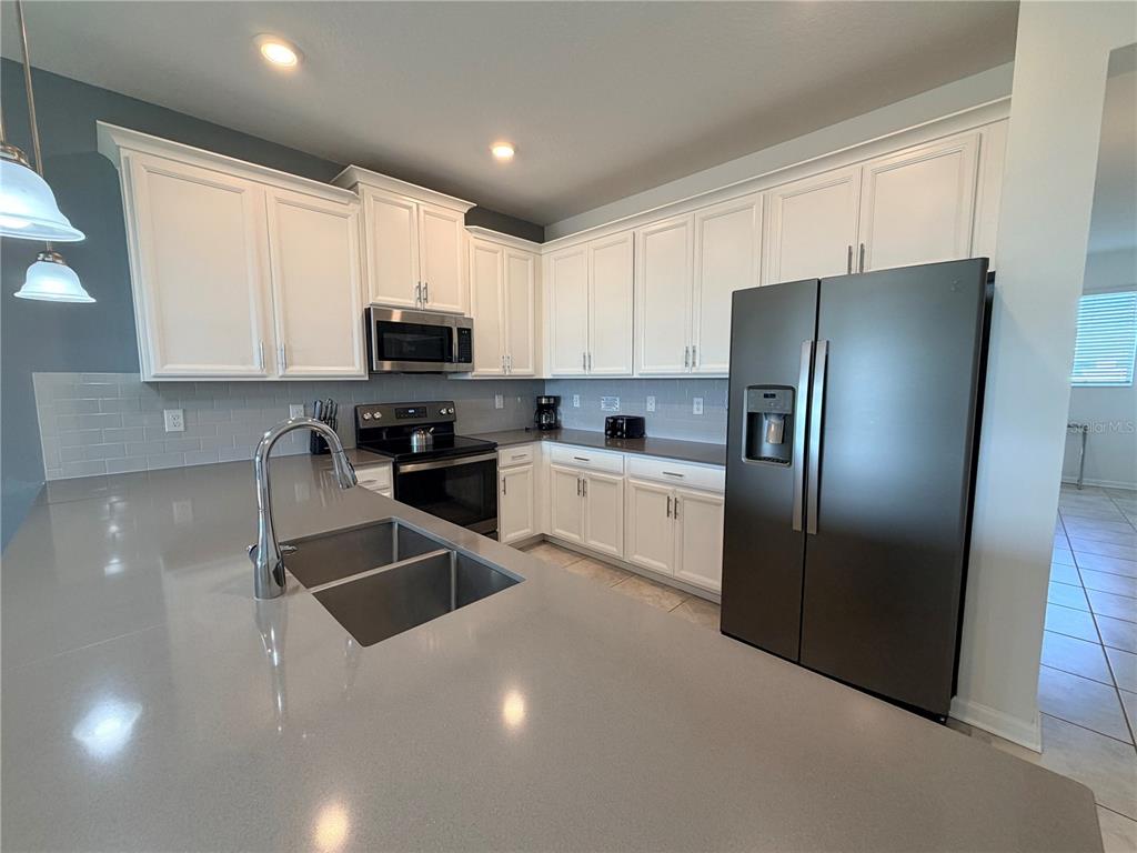 A kitchen features white cabinets, gray quartz countertops, stainless steel appliances, and a double sink — 1115 CHALLENGE DRIVE UNIT 1115, DAVENPORT, FL