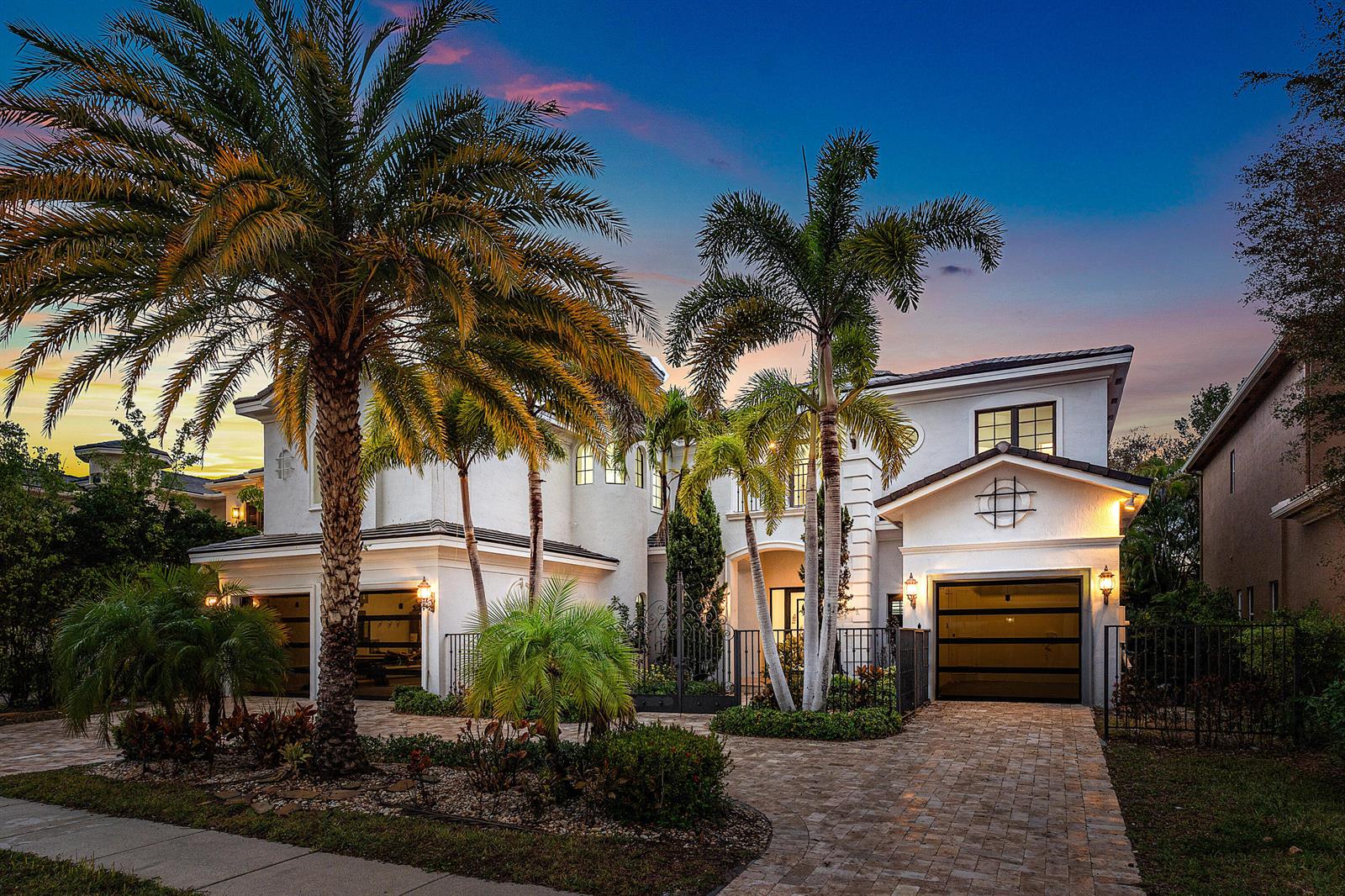 A two-story white house with palm trees, a paved driveway, and multiple garage doors at dusk — 17606 Circle Pond Court, Boca Raton FL 33496, BOCA RATON, FL