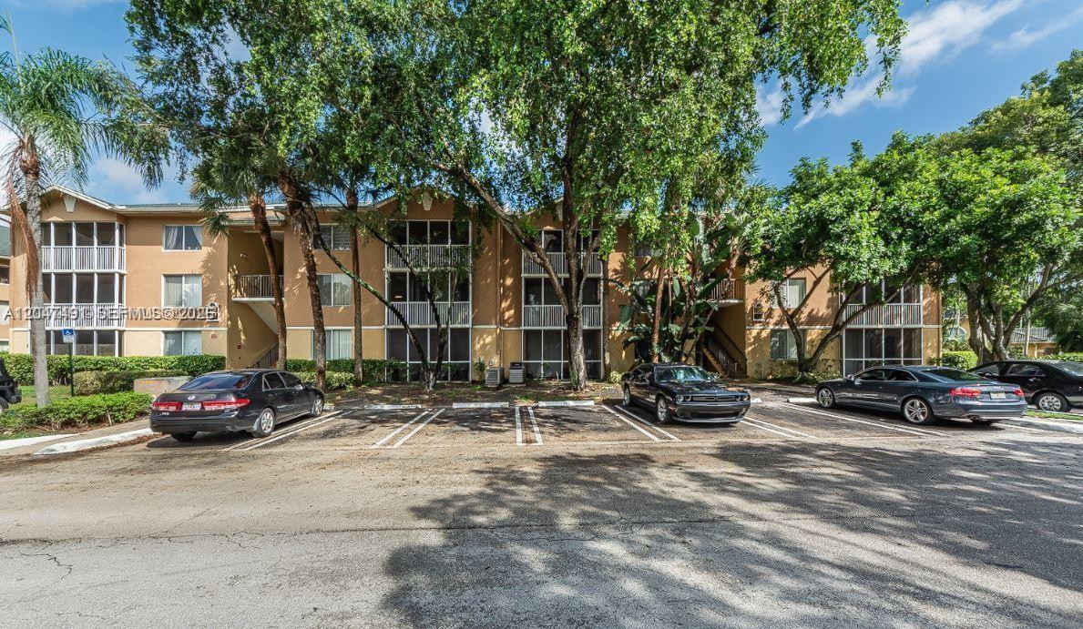A three-story apartment building with screened balconies sits behind a paved parking lot — POMPANO BEACH, FL