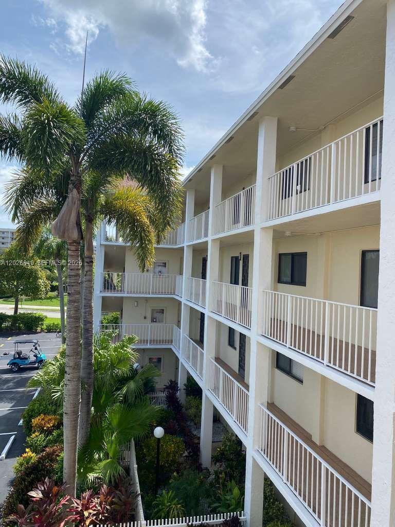 An exterior view of a multi-story apartment building with white railings and palm trees — 7350 Kinghurst Dr # 305, Delray Beach FL 33446, DELRAY BEACH, FL